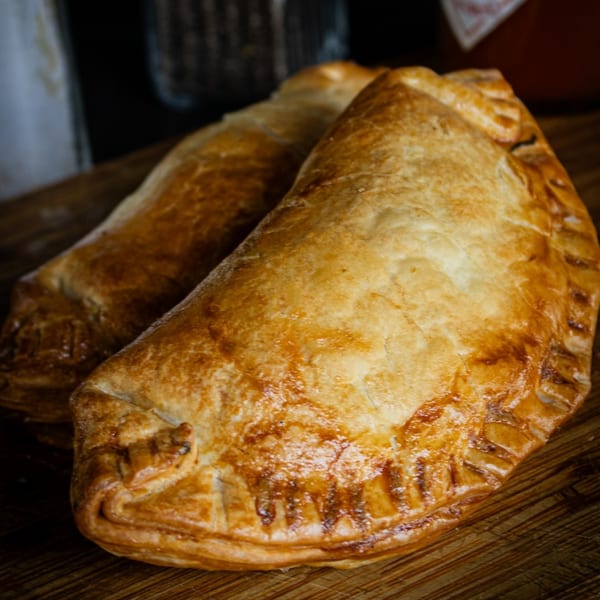 Two golden-brown, flaky pastries, possibly empanadas or pasties, resting on a wooden surface.