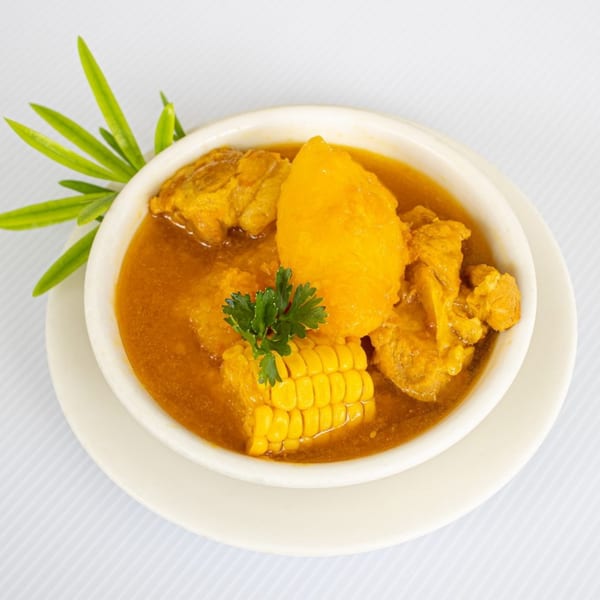 Hearty stew with chicken, corn on the cob, and yellow potatoes, garnished with parsley.