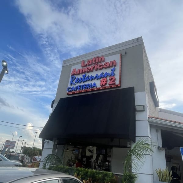 Exterior of Latin American Restaurant Cafeteria #2 with a black awning under a blue sky.