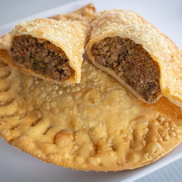 Two golden-brown, crispy empanadas filled with savory ground meat, one cut open to show the filling.