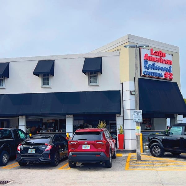 Exterior of Latin American Restaurant Cafeteria #2 with black awnings and parked cars.