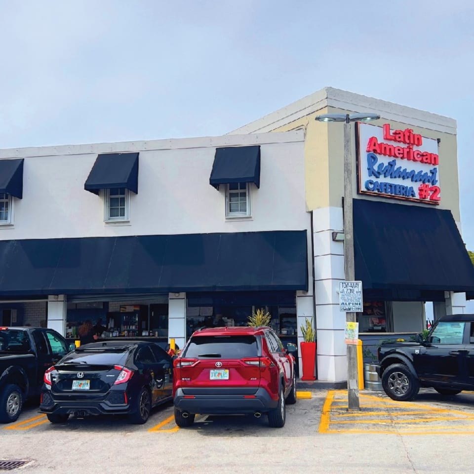 Exterior of Latin American Restaurant Cafeteria #2 with black awnings and parked cars.