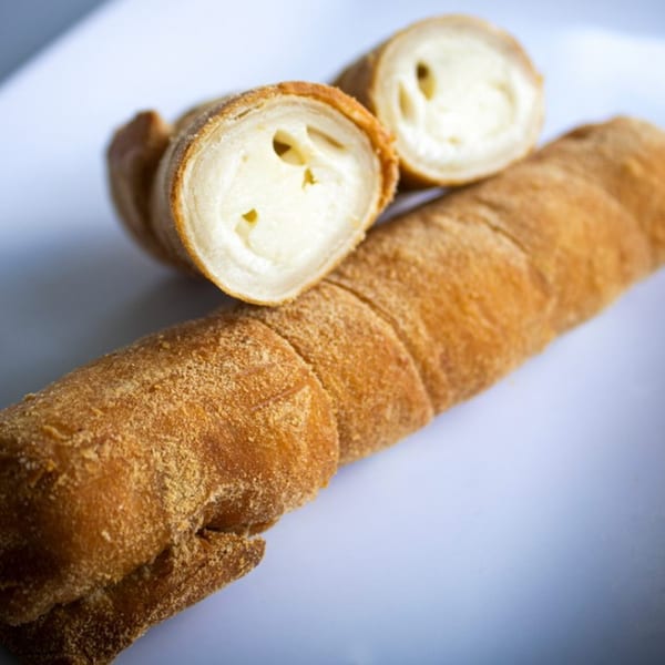 Close-up of a golden-brown pastry roll, cut open to reveal a creamy white filling.