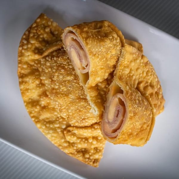 Golden fried pastry, one whole and one cut open revealing ham and cheese filling.