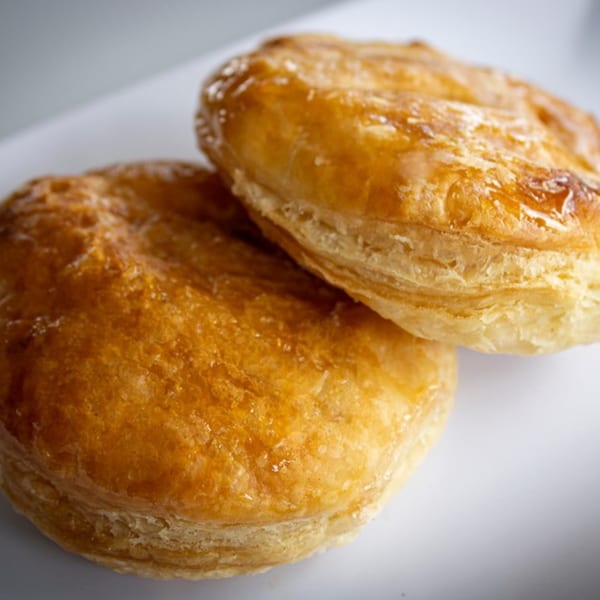 Two golden-brown, flaky biscuits with a shiny glaze, stacked on a white plate.