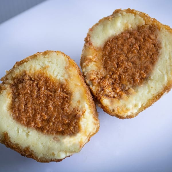 Two halves of a fried potato ball, revealing a savory meat filling inside.