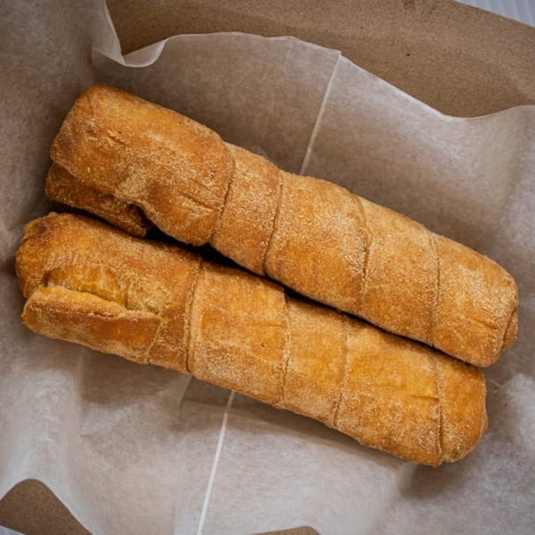 Two golden-brown, crispy tequeños, a Venezuelan cheese stick, resting in a paper-lined basket.