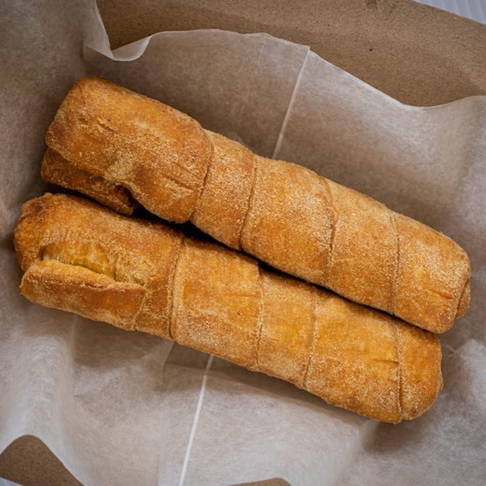 Two golden-brown, crispy tequeños, a Venezuelan cheese stick, resting in a paper-lined basket.