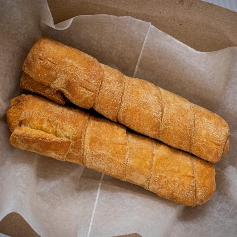 Two golden-brown, crispy tequeños, a Venezuelan cheese stick, resting in a paper-lined basket.