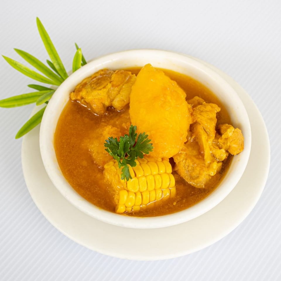 Hearty stew with chicken, corn on the cob, and large yellow potatoes, garnished with parsley.