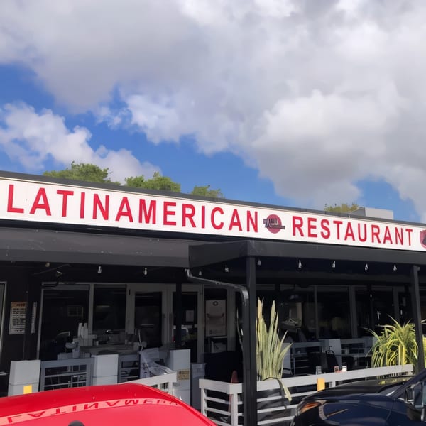 Exterior of a Latin American restaurant with a red sign, black awning, and outdoor seating.