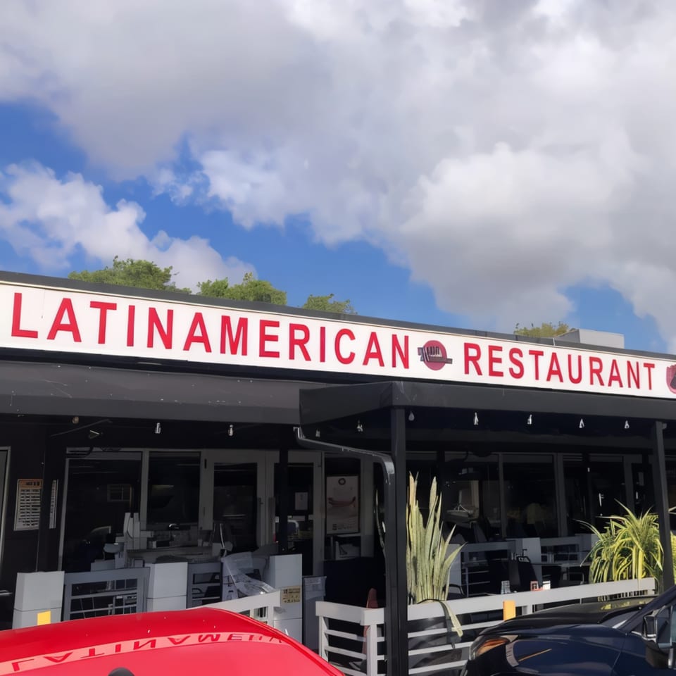 Exterior of a Latin American restaurant with a red sign, black awning, and outdoor seating.