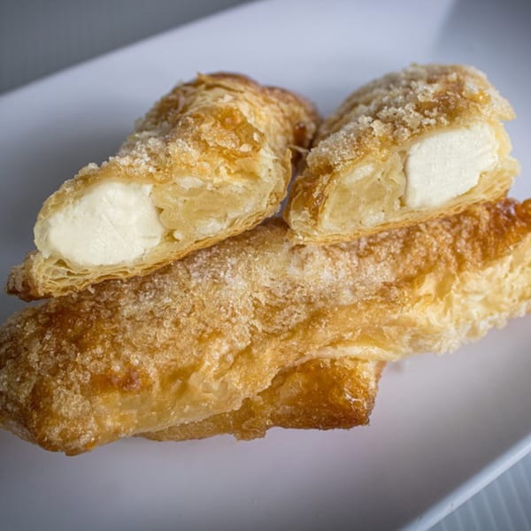 Three golden-brown pastries, two cut open to reveal creamy white filling, on a white plate.